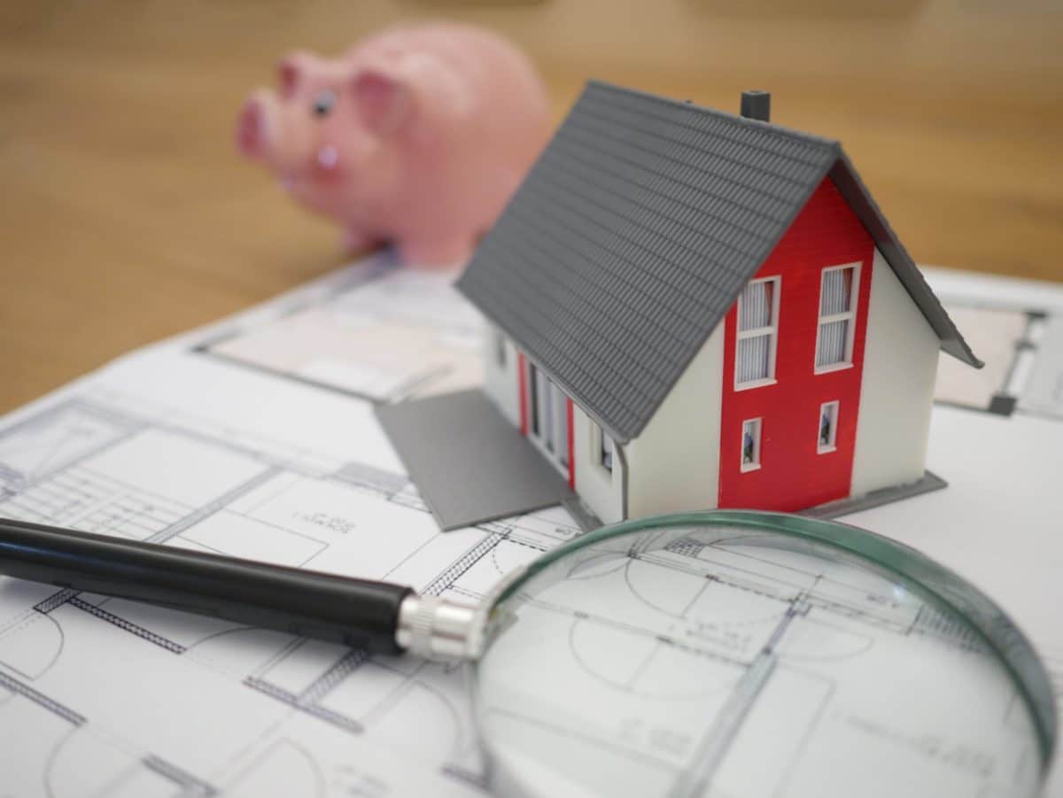 magnifying glass with miniature house and piggybank on top of CPF money forms